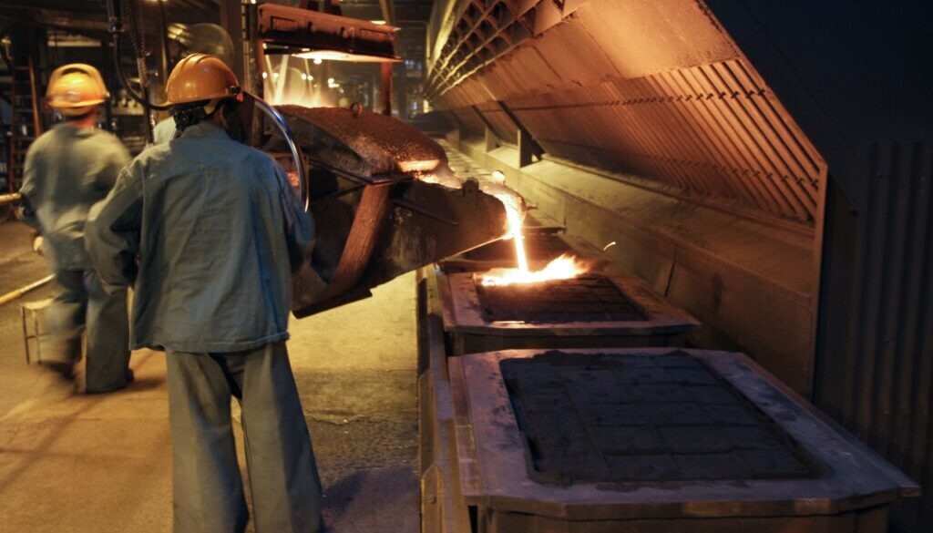 Foundry workers wearing protective gear carefully pour molten metal into molds to create gray iron castings.