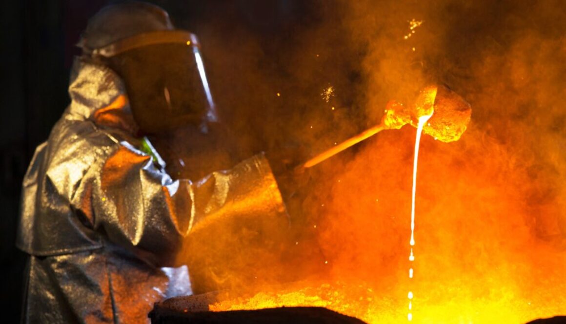 An iron foundry worker wearing protective gear pours molten metal.